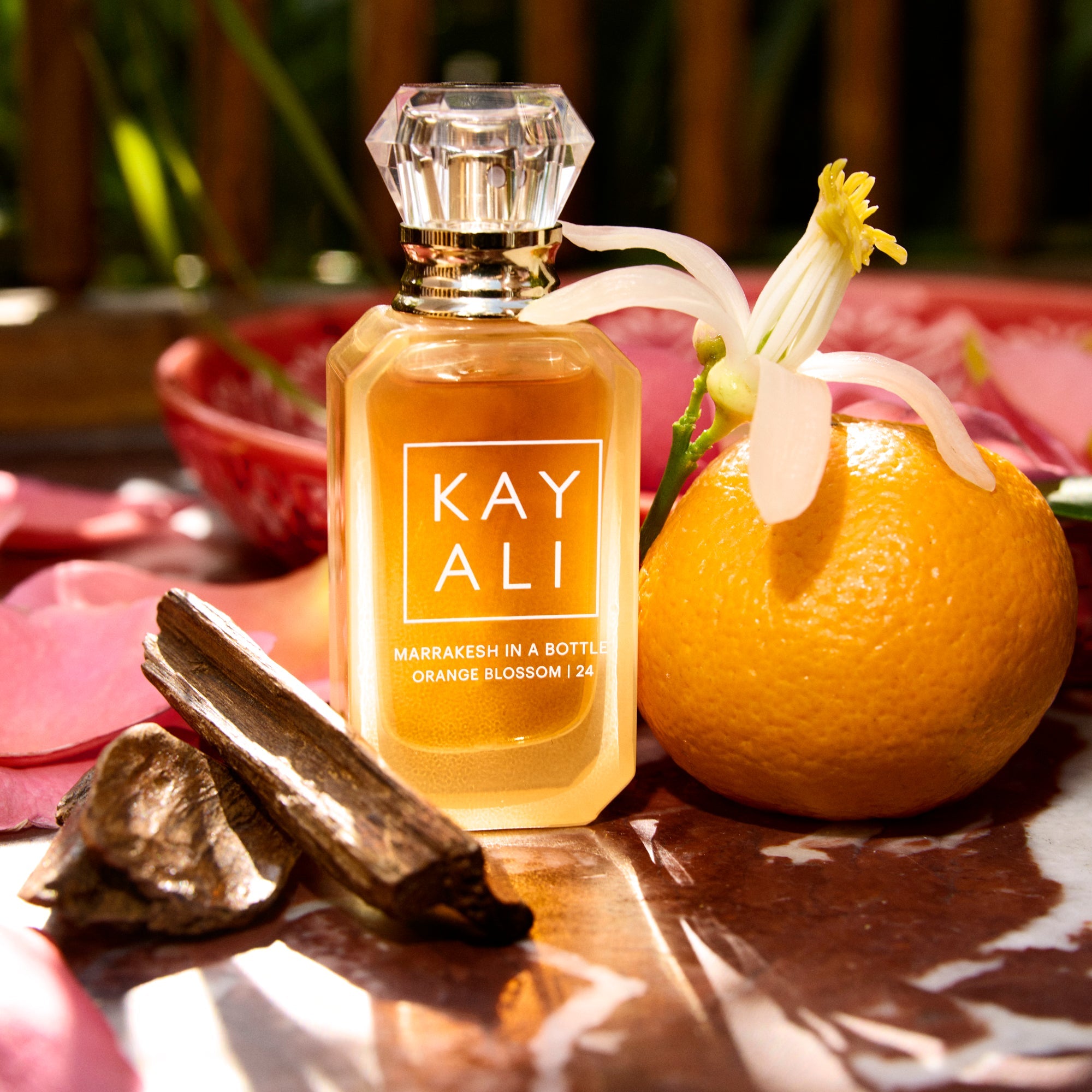 Perfume bottle labeled 'KAYALI' with an orange and floral elements on a reflective surface.